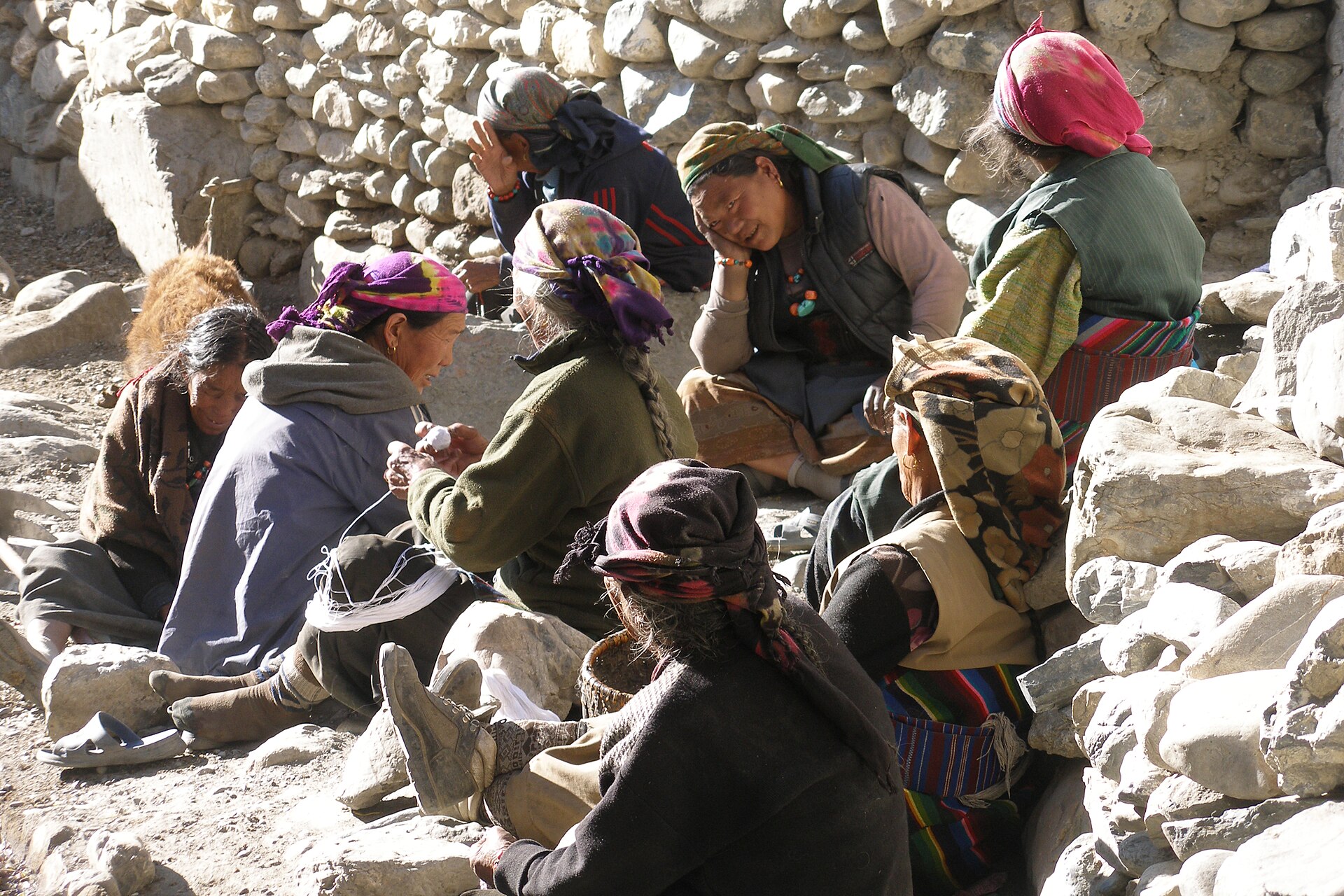 Women of Kagbeni sitting by a stone wall spinning wool together